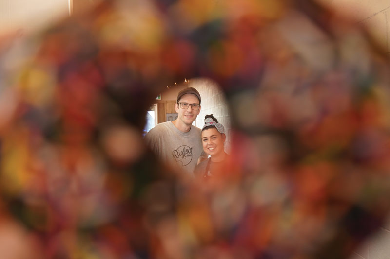 Bigfoot Donuts owners seen through the hole of a chocolate sprinke donut
