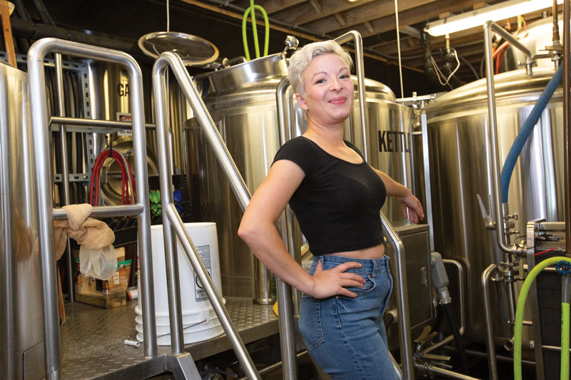 Craft Brewing program alum, Elie Hadley, stands in the brewhouse at her place of work.