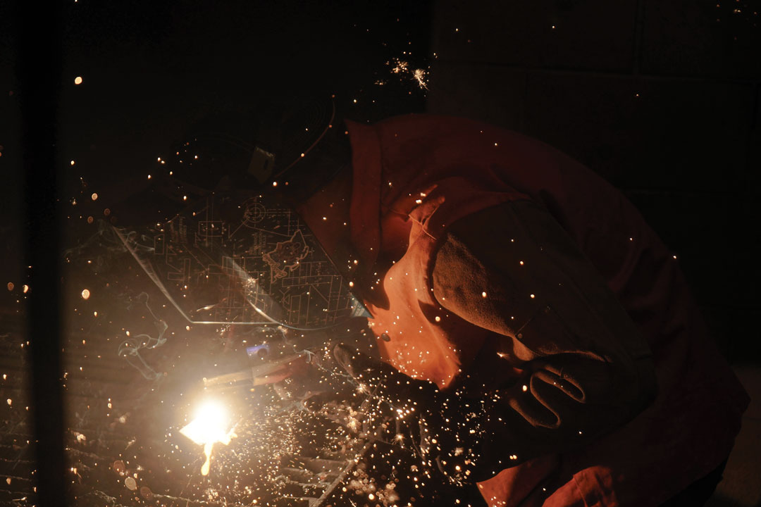 Welding student in protective gear uses torch, sparks fly. 