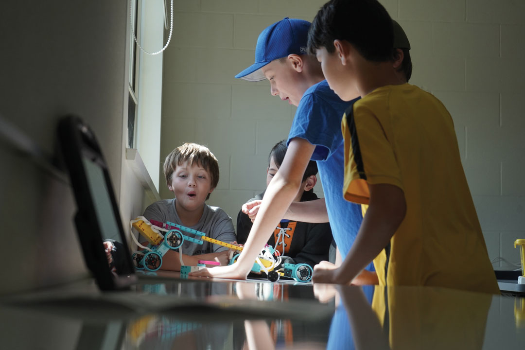 A group of youth academy students look surprised by the robot they've built.