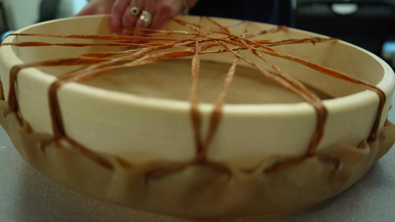 A close up image of hands tying animal hide to a traditional drum