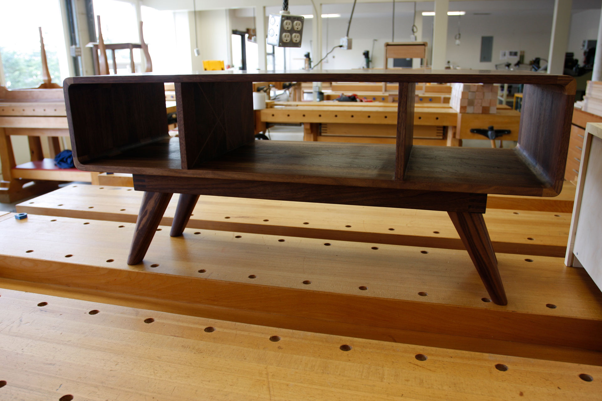 A midcentury-inspired table is displayed on a workbench in the trades shop