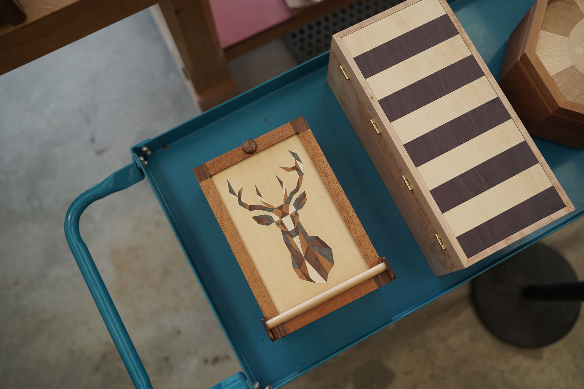 Small intricately-designed wooden boxes created by students are displayed on a rolling cart.