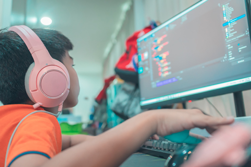 Child sits in front of a computer using coding software. They are wearing headphones. 
